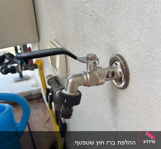ברז מים מותקן על קיר עם צינור צהוב